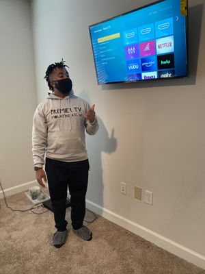 Premier TV Mounting Atl — Marcus in a branded Premier TV Mounting Atl hoodie presenting a mounted Samsung TV with the Roku home screen
