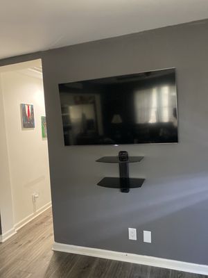Premier TV Mounting Atl — large flat-panel TV with lower game shelf installed on a grey accent wall in a residential living room